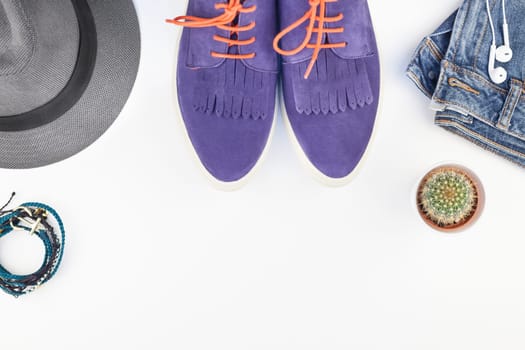 Flat lay of suede shoes, blue jeans, grey hat, cactus and smartphone with headphones on white background with copy space. Overhead view of woman casual outfit. Trendy hipster look top view