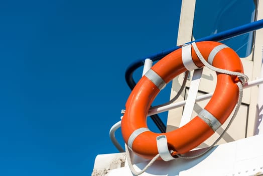 Bright orange lifebuoy on a white yacht side. Blue sky background