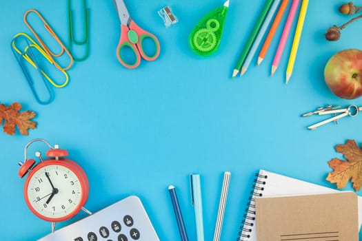 Creative flat lay top view back to school concept with alarm clock, color school and office supplies on bright turquoise paper table frame background with copy space, template for text or design