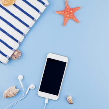 Creative square flat lay concept of summer travel vacations. Top view of beach towel, seashells, starfish and smartphone on pastel blue background with copy space in minimal style, template for text