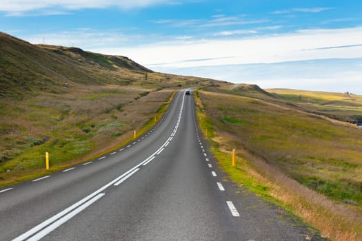 Highway through Icelandic landscape under a blue summer sky. Horizontal shot