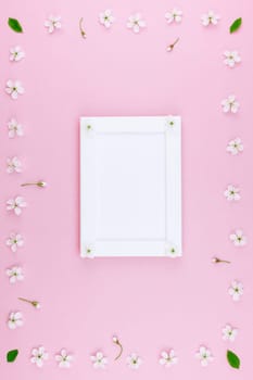 Creative flat lay concept top view of blank frame mock up and cherry tree flowers on pastel millennial pink background with copy space in minimal style, template for lettering, text or design