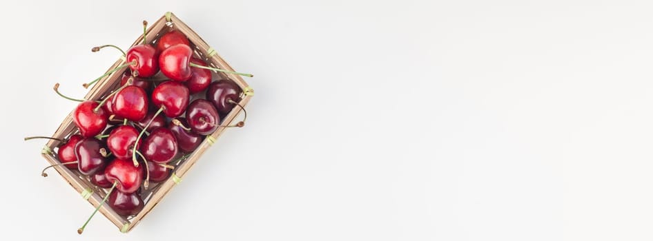 Long wide banner of fresh ripe cherry in a small wicker basket with copy space isolated white background minimal style. Concept of summer fun and healthy eating. Template for your text or food design