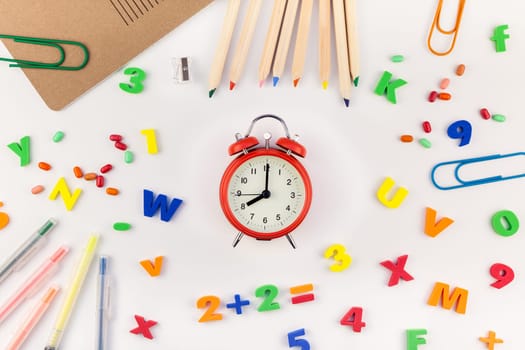 Creative flat lay back to school concept with alarm clock, color school and office supplies on white table background with copy space, frame, template for text or design