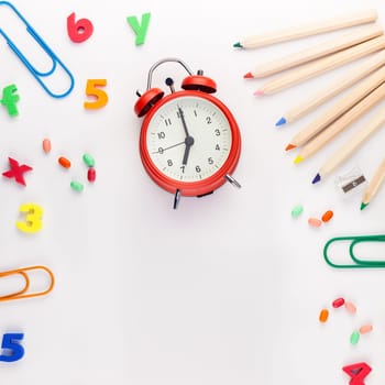 Square flat lay back to school concept with alarm clock, color school and office supplies on white table background with copy space, frame, template for text or design