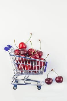 Creative image of ripe cherries in a shopping cart with copy space isolated on white background in minimal style. Concept of supermarket or fruit market shopping. Template for your text or design.
