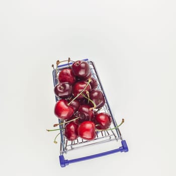 Square top view of ripe cherries in a shopping cart with copy space isolated on white background in minimal style. Concept of supermarket or fruit market shopping. Template for your text or design.