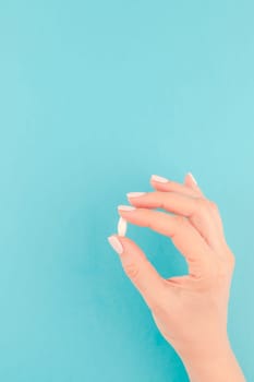Woman hand holding a white pill on pastel blue paper background with copy space in minimal style, template for text. Concept of medical treatment, pharmacy, healthcare.