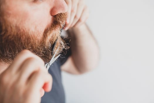 Selfcare during quarantine isolation. Adult handsome caucasian man cutting moustache and beard himself personally with scissors at home. Coronavirus outbreak and people shutdown, stay home concept