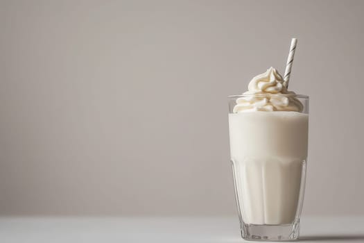 A sleek, clear glass filled with a creamy milkshake topped with whipped cream and a striped straw sits elegantly against a soft, neutral background, highlighting its minimalist design.