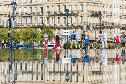 FRANCE, BORDEAUX - SEPTEMBER 20: People riding bicycles in the mirror fountain in front of Place de la Bourse in Bordeaux, France on September 20, 2015