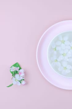 Creative flat lay concept top view of aroma bowl with water and white spring blossoming apple tree flowers on pastel pink paper background with copy space in minimal style, template for text