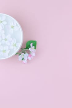 Creative flat lay concept top view of aroma bowl with water and white spring blossoming apple tree flowers on pastel pink paper background with copy space in minimal style, template for text