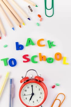 Creative flat lay back to school concept with alarm clock, color school and office supplies on white table background with copy space, frame, template for text or design