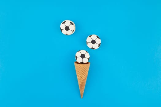 Creative flat lay top view of ice cream waffle cones with soccer balls macarons on bright bold blue background with copy space in minimal style, concept of football games for children birthday