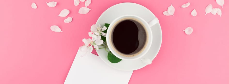 Creative flat lay concept top view of coffee cup and white apple tree flowers petals on pastel pink background with postcard mock up and copy space in minimal style template for text. Long wide banner