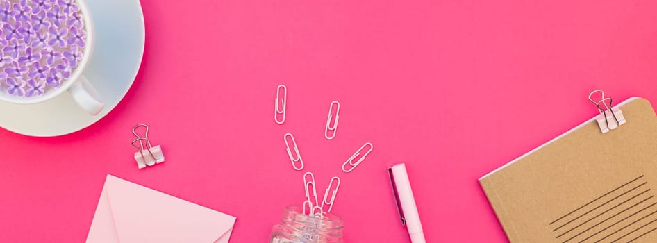 Creative top view flat lay of workspace desk styled design office supplies and cup of tea with copy space on a bright pink color paper long wide banner. Template for feminine blog social media