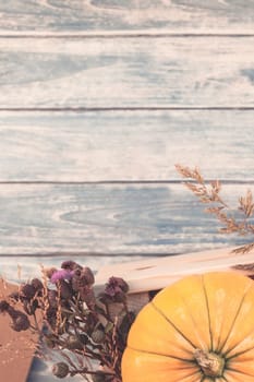 Top view of autumn orange pumpkins and dry flowers and grass in box thanksgiving background over blue toned wooden table with copy space. Template for fall harvest mood text