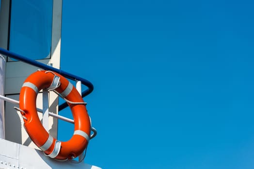 Bright orange lifebuoy on a white yacht side. Blue sky background