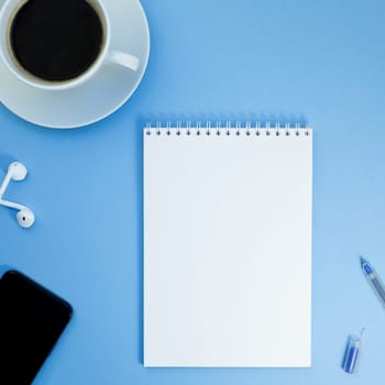 Creative square flat lay photo of workspace desk with paper notebook, smartphone, earpieces, pen and coffee with copy space background minimal style
