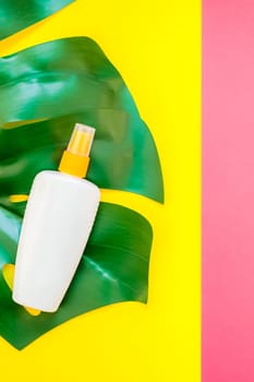 Tropical jungle palm monstera leaves and sunscreen blank bottle mockup on bright yellow and pink duotone paper background. Summer vacations creative flat lay concept template for text