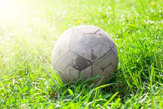 Old soccer ball forgotten in the green grass field. The football concept