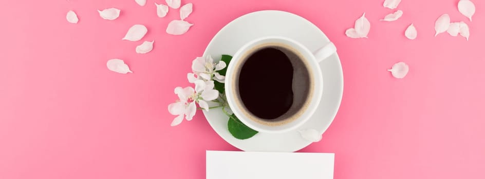 Creative flat lay concept top view of coffee cup and white apple tree flowers petals on pastel pink background with postcard mock up and copy space in minimal style template for text. Long wide banner