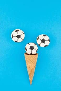 Creative flat lay top view of ice cream waffle cones with soccer balls macarons on bright bold blue background with copy space in minimal style, concept of football games for children birthday