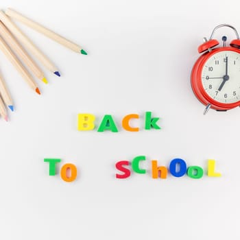Square flat lay back to school concept with alarm clock, color school and office supplies on white table background with copy space, frame, template for text or design