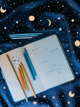 Open journal with pencils on a starry night-themed fabric, evoking creativity and imagination.