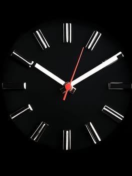 Minimalist black wall clock with white markings and red second hand against dark background. Modern timepiece design showing almost midnight.