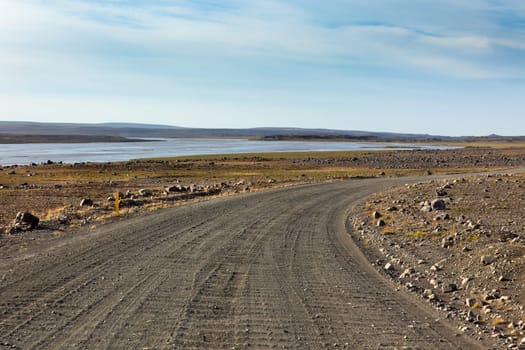 Iceland Dirt Road through Stone Field and a River. Bright Blue Sky