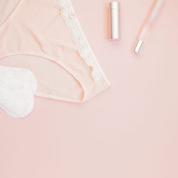 Square Feminine flat lay set of female panties and accessories, perfumes, lipstick and pads liners on pastel pink color background for fashion blog and social media with copy space for text