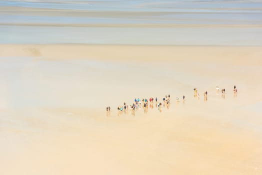 View from walls of Mont Saint Michel on the bay during the low tide with groups of tourists walking. France