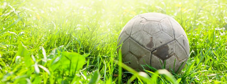 Old soccer ball forgotten in the green grass field. The football concept. Long wide banner