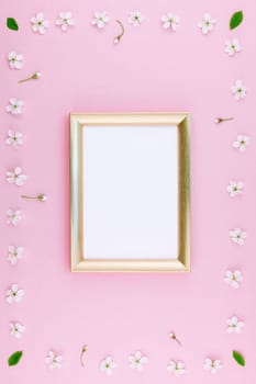 Creative flat lay concept top view of blank frame mock up and cherry tree flowers on pastel millennial pink background with copy space in minimal style, template for lettering, text or design