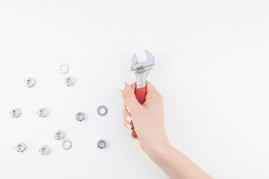 Creative image of woman hand with pastel manicure polish holding spanner with copy space and nuts isolated on white background in minimalism style. Repair or improvement feminism concept