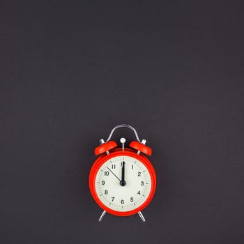 Concept image of a red vintage alarm clock with twelve o clock on dark black color paper background with copy space in minimal style, square template for text