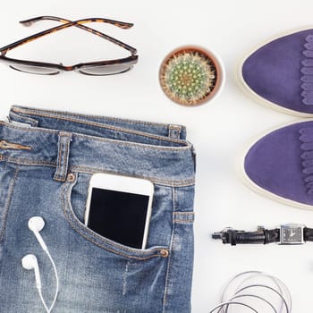 Square Flat lay of suede shoes, blue jeans, bracelets cactus and smartphone with headphones on white background with copy space. Overhead view of woman casual outfit. Trendy hipster look top view