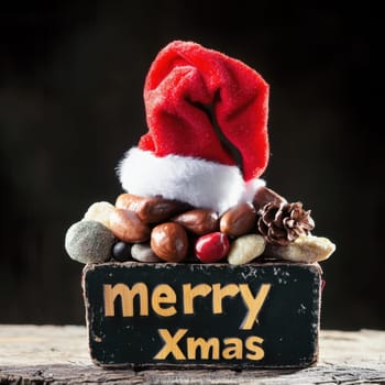 A joyful display of pebbles and nuts topped with a red Santa hat and a cheerful sign wishing Merry Xmas in the holiday spirit.