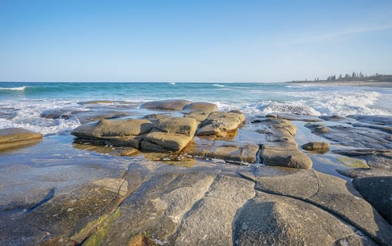 Looking south along Buddina Beach with ocean waves breaking over the rocky foreshore platform as the surf rolls in at Point Cartwright, Sunshine Coast, Queensland.