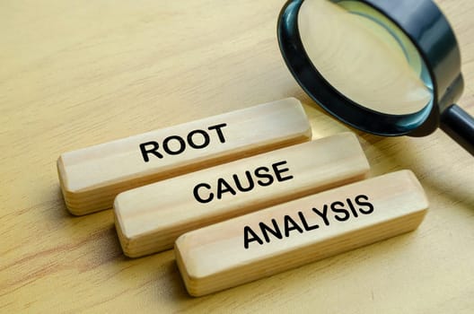Root Cause Analysis text on wooden blocks with magnifying glass background.