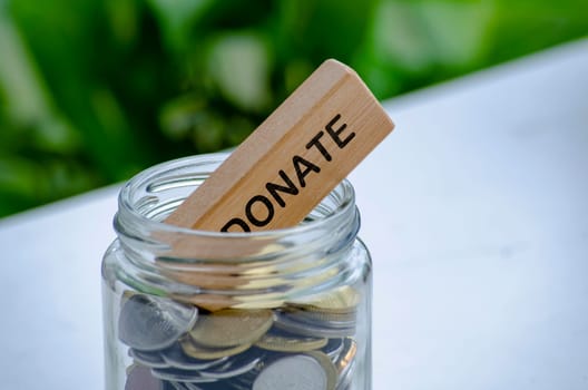 Donate text on wooden block inside a jar with golden coins. Charity and conservation concept.