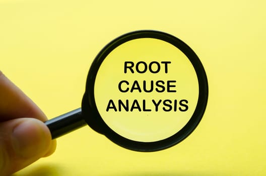 Hand holding magnifying with Root Cause Analysis text on yellow background. Investigation and solution concept.
