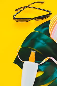 Tropical jungle palm monstera leaves, sunglasses, sunscreen blank bottle mockup and woman's swimsuit top on bright yellow paper background. Summer vacations creative flat lay concept template for text
