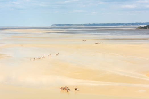 View from walls of Mont Saint Michel on the bay during the low tide with groups of tourists walking. France