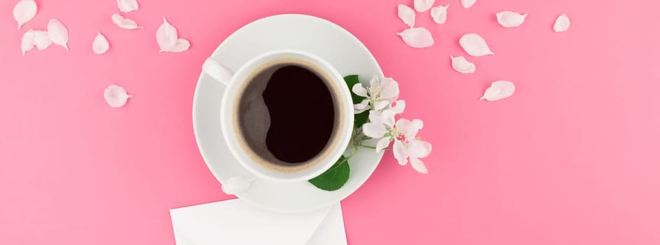 Creative flat lay concept top view of coffee cup and white apple tree flowers petals on pastel pink background with postcard mock up and copy space in minimal style template for text. Long wide banner