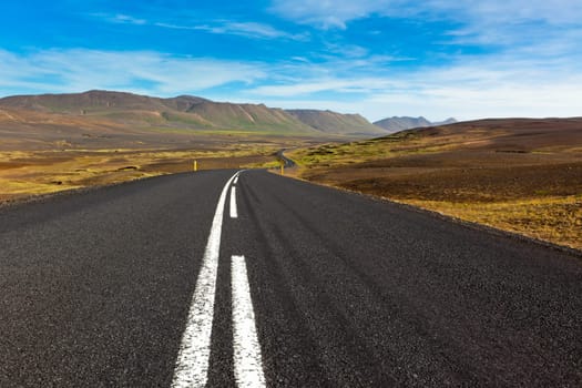 Highway through dry gravel lava field landscape under a blue summer sky. Highlands of Central Iceland.