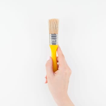 Square image of woman hand holding new paint brush with copy space isolated on white background in minimalism style. Template for feminine blog, social media. Repair or improvement concept