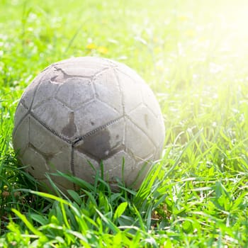 Old soccer ball forgotten in the green grass field. The football concept. Square shot